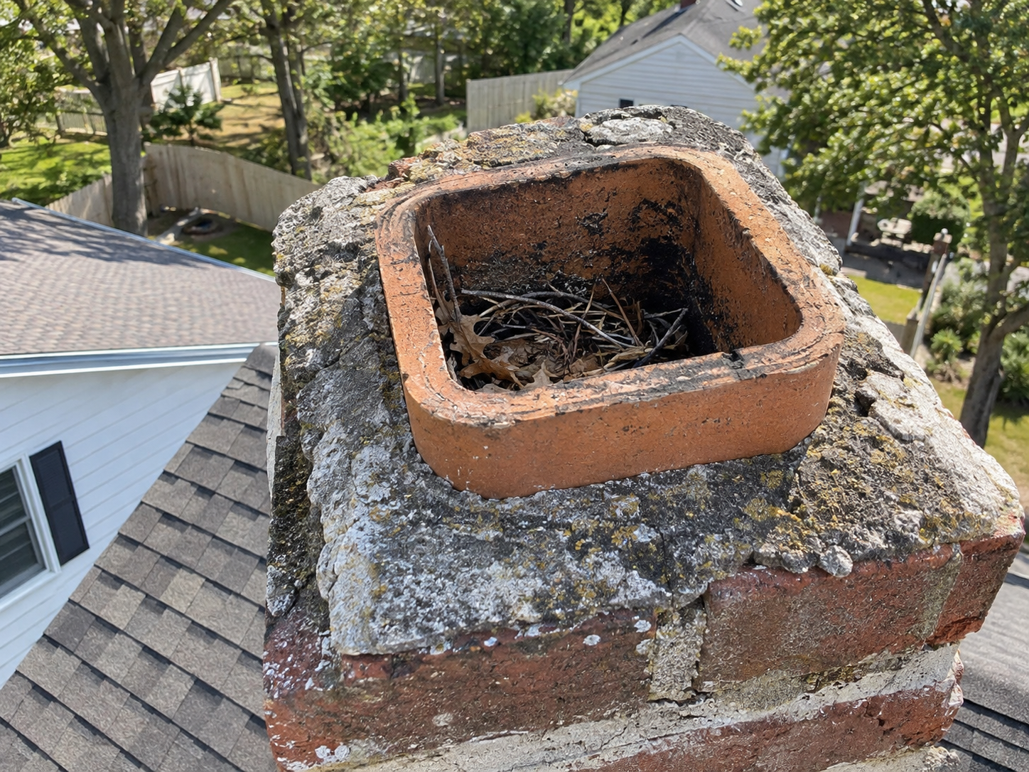 Uncapped chimney with an open clay flue tile filled with a bird nest, twigs and leaves